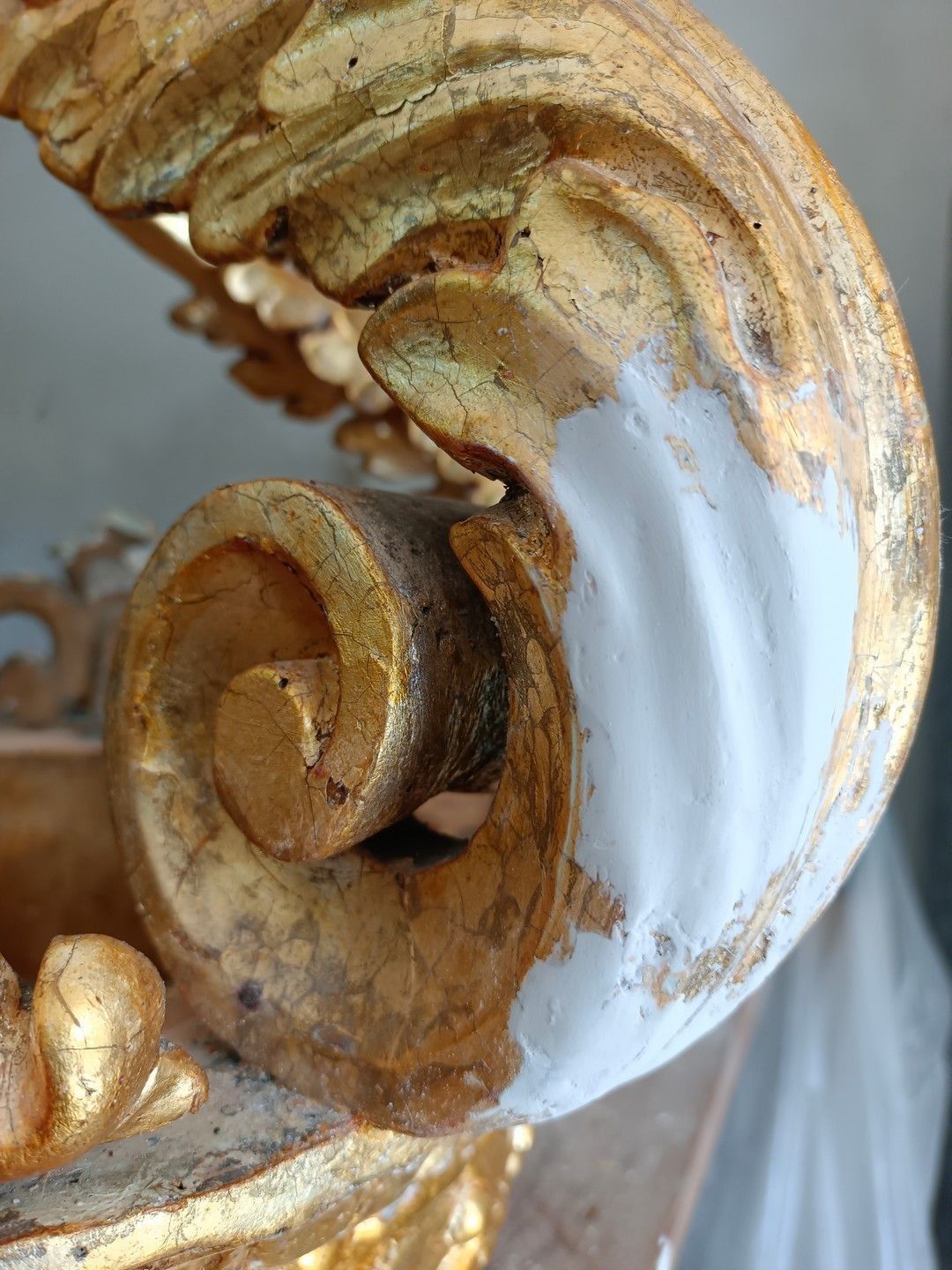 Primo piano di una spirale decorativa dorata e bianca, consumata dal tempo, su una parete o una colonna.