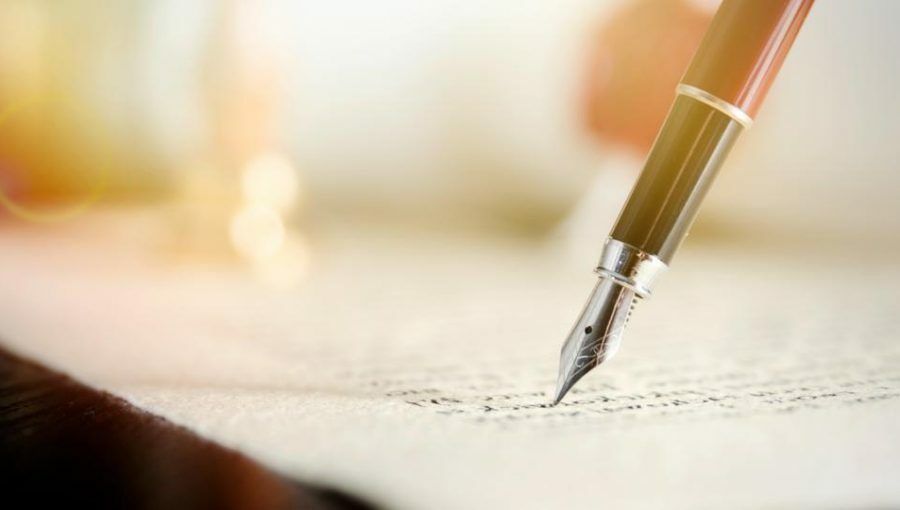 A person is writing with a fountain pen on a piece of paper.