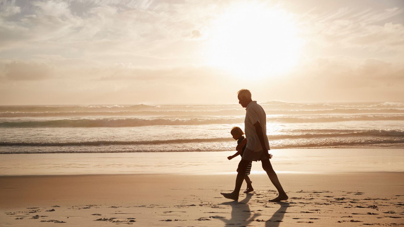 A man and a child are walking on the beach at sunset.