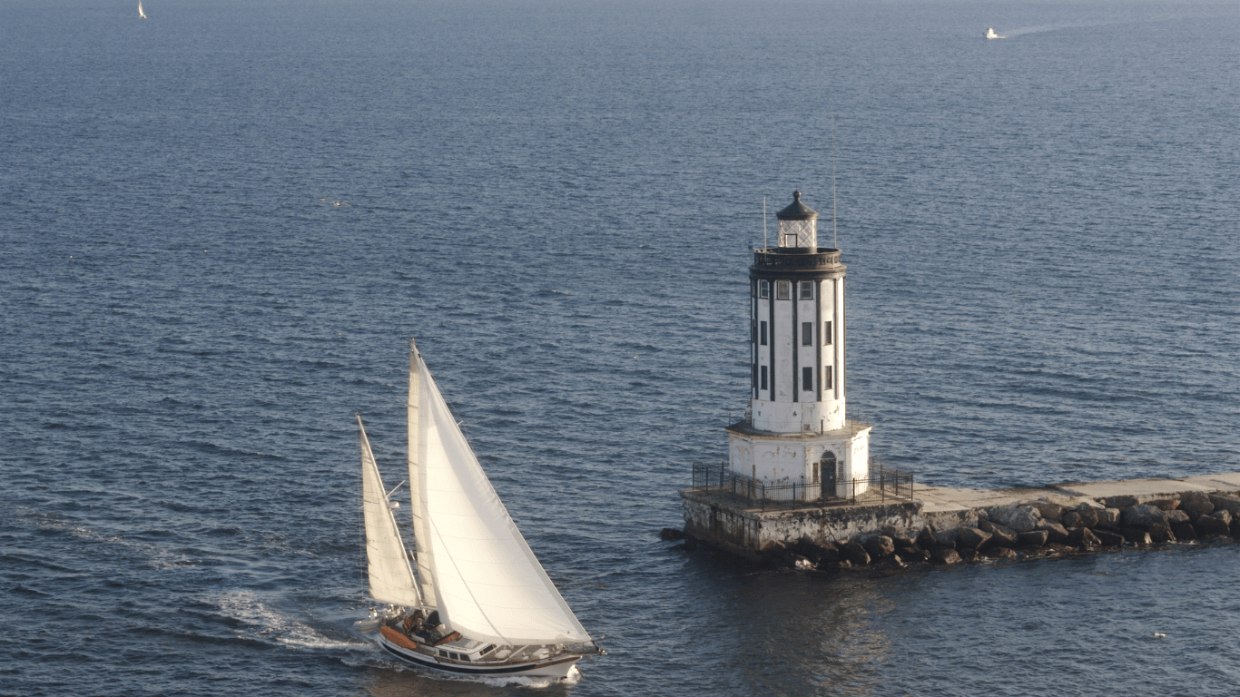 A sailboat is sailing past a lighthouse in the ocean.