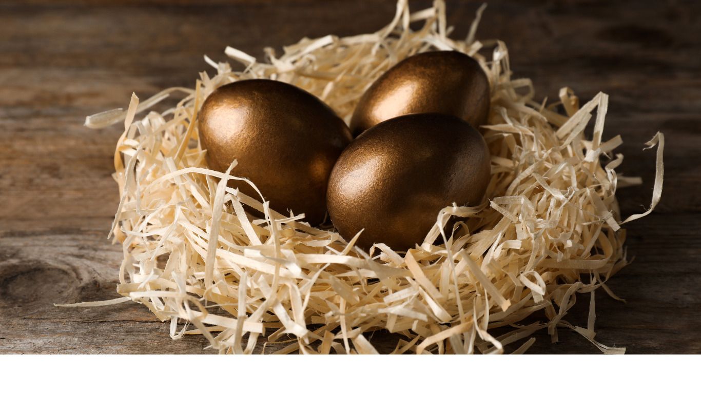 Three gold eggs are sitting in a nest of hay on a wooden table.