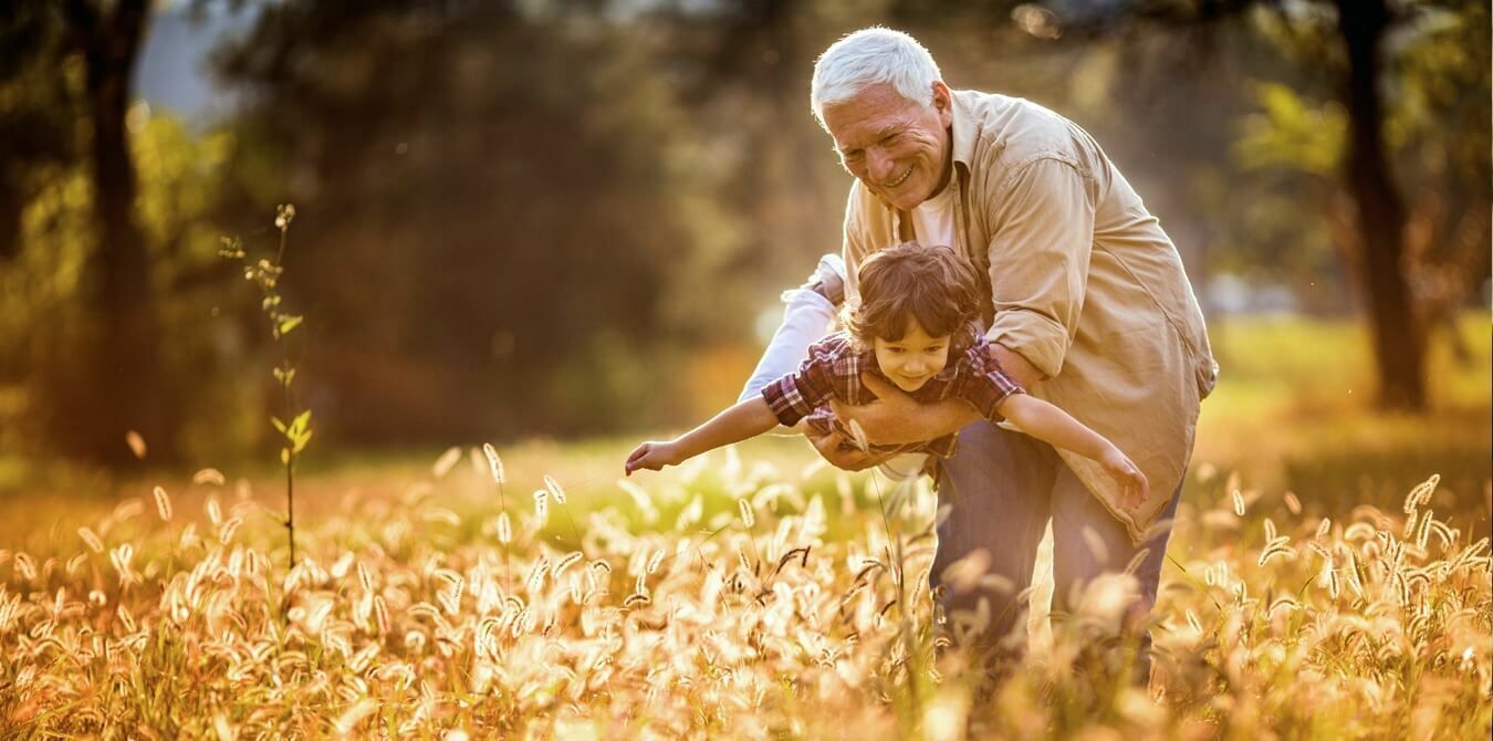 An elderly man is giving a child a piggyback ride in a field.