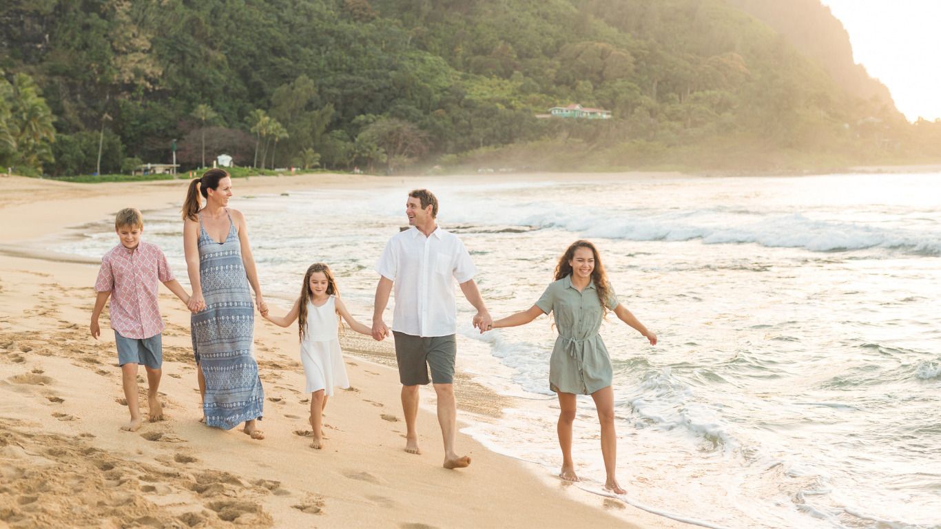 A family is walking along the beach holding hands.