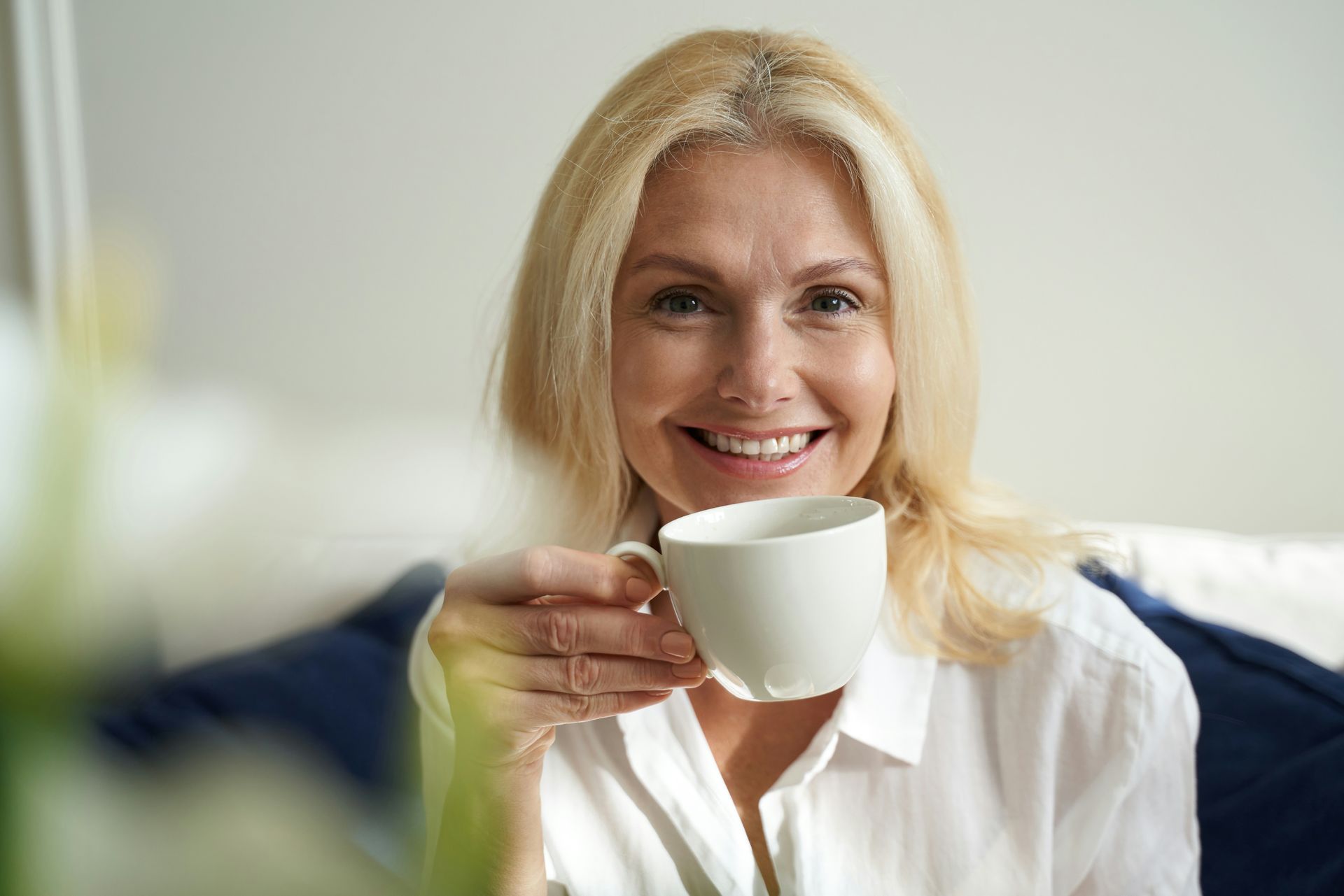 A woman is sitting on a couch drinking a cup of coffee.