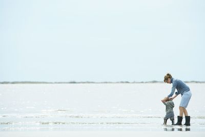 A woman is holding a baby on the beach.