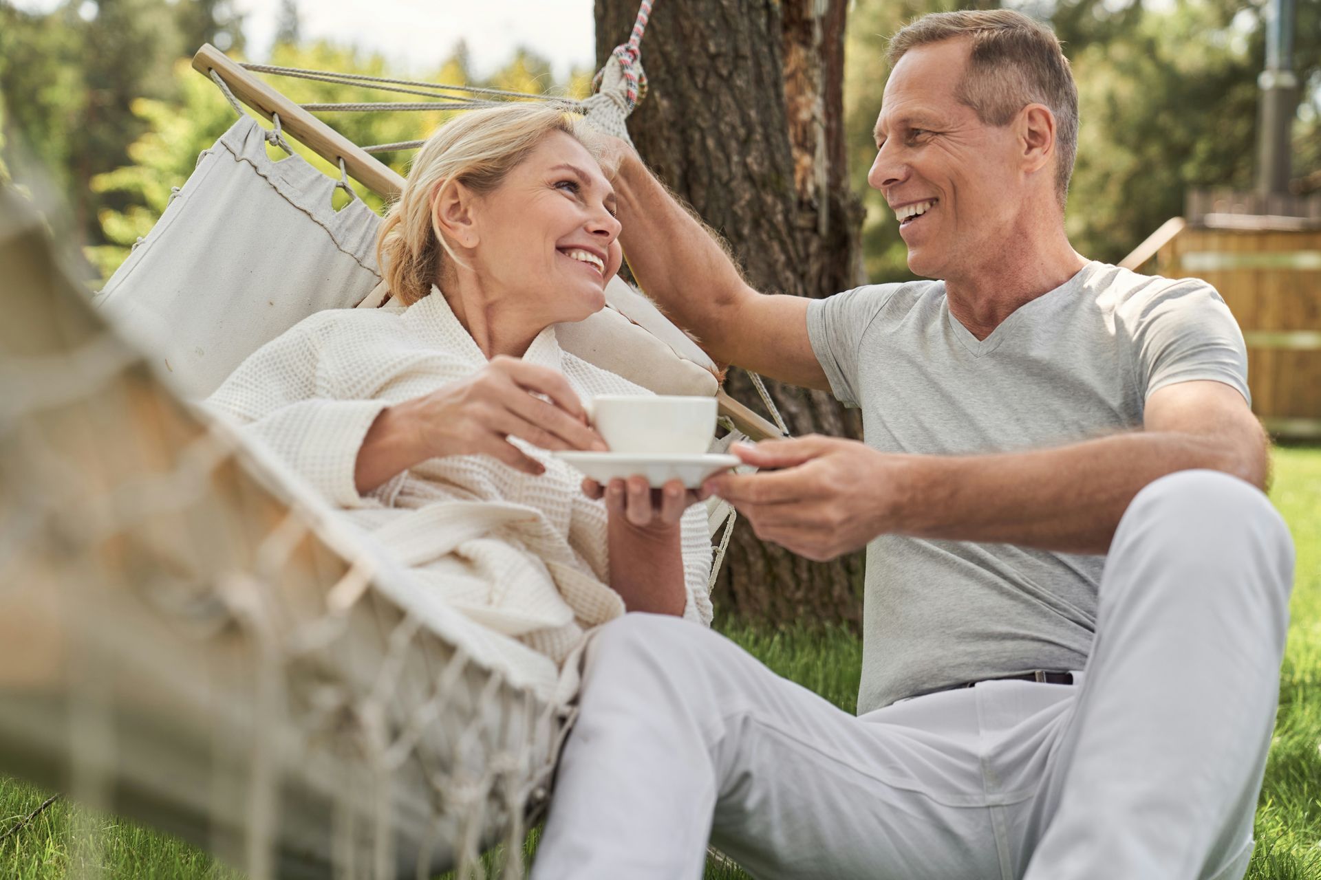 A man and a woman are sitting in a hammock drinking coffee.