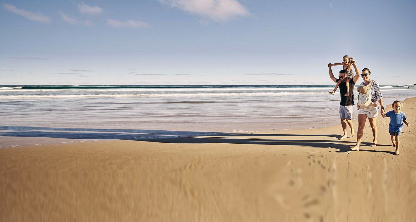 A family is walking on the beach holding hands.