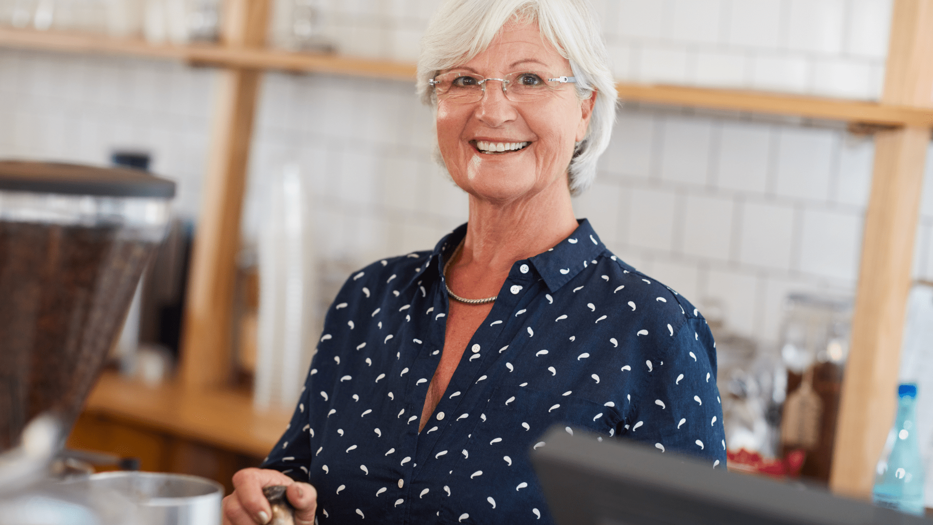 An older woman is smiling while standing at a counter in a kitchen.