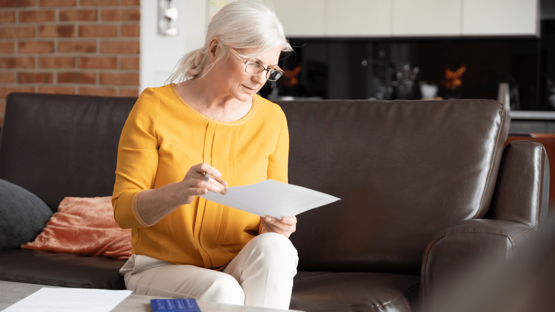 An elderly woman is sitting on a couch looking at a piece of paper.
