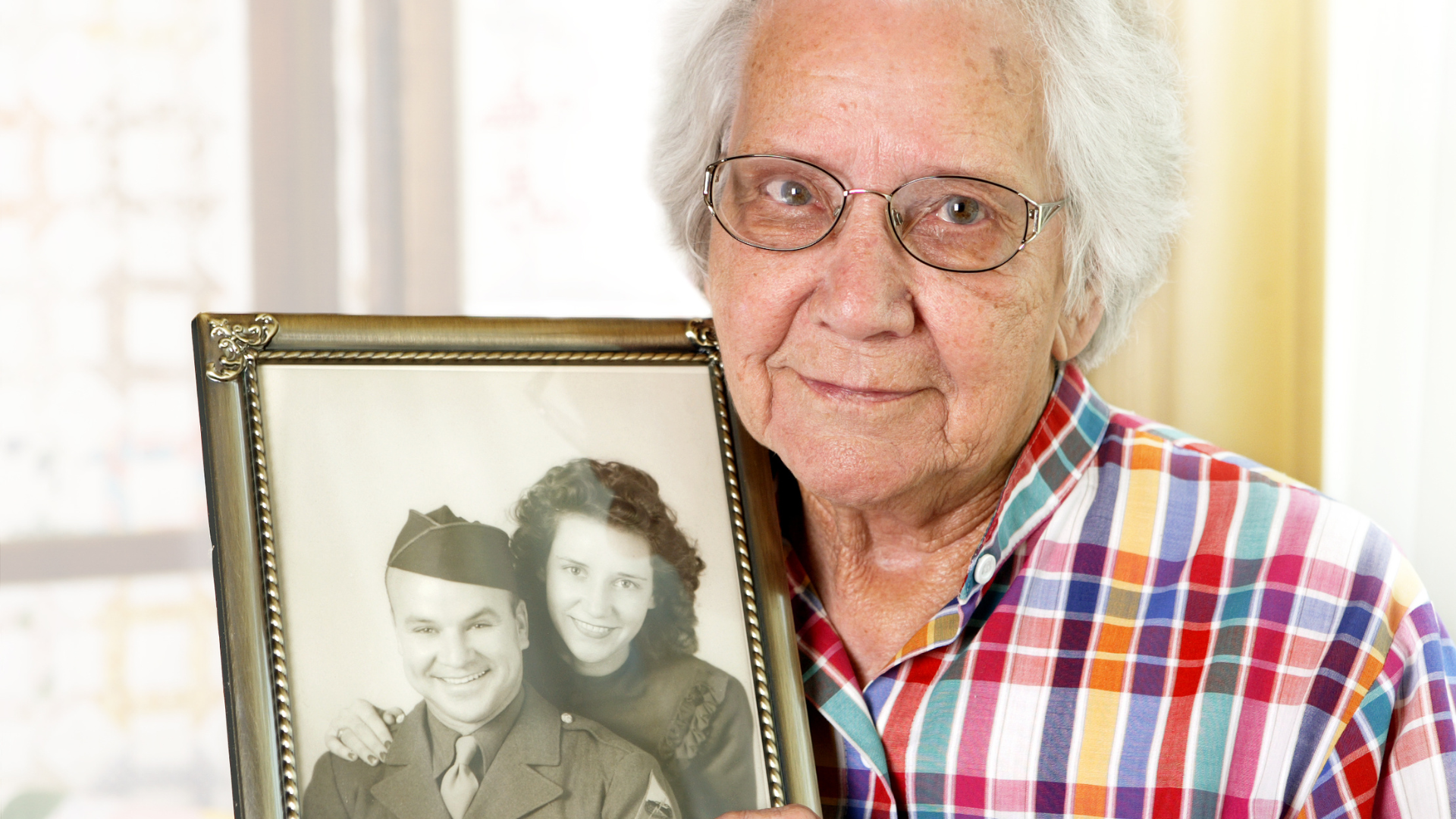 An elderly woman is holding a framed picture of a man and woman.
