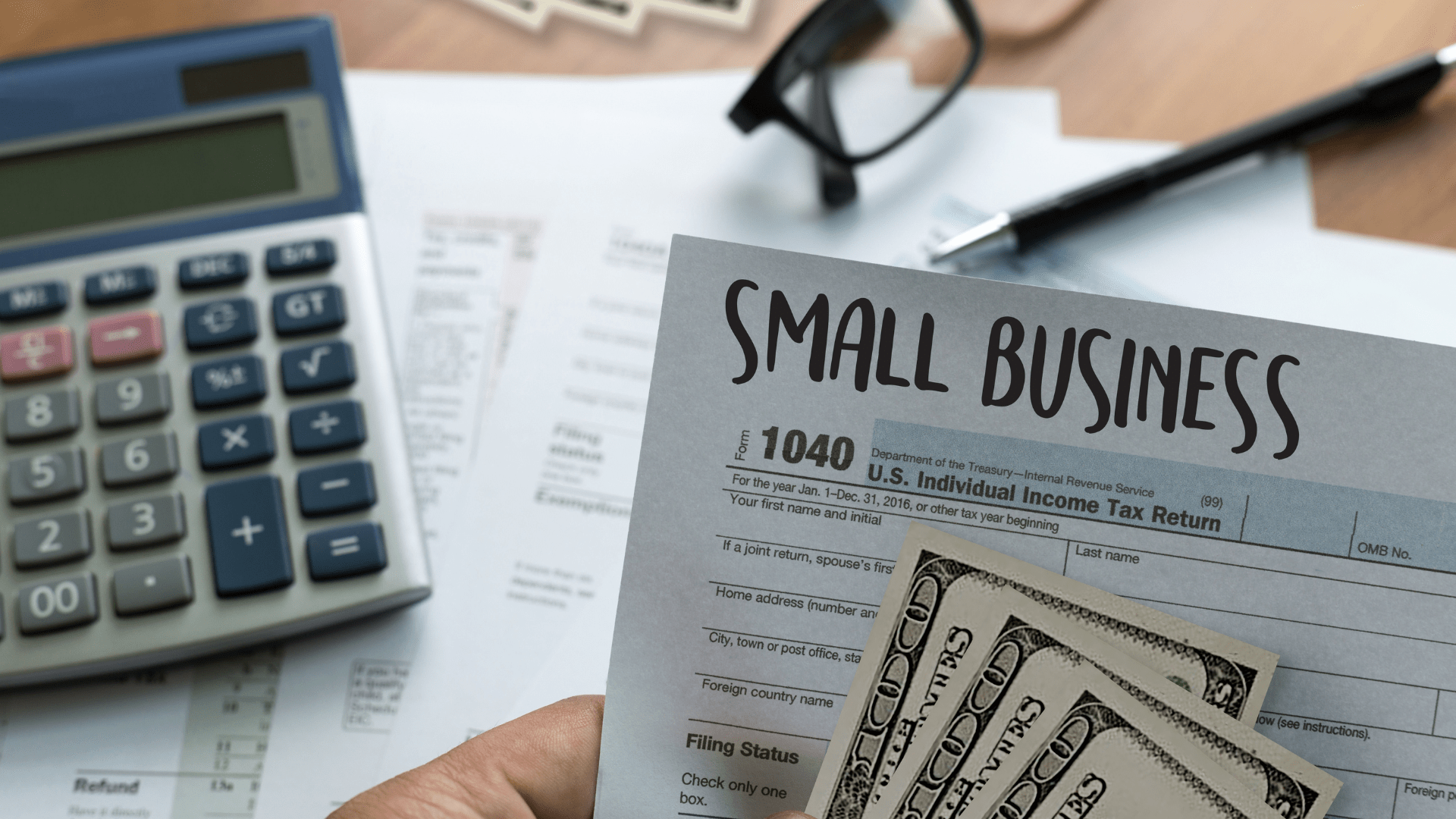A person is holding a small business tax form next to a calculator.
