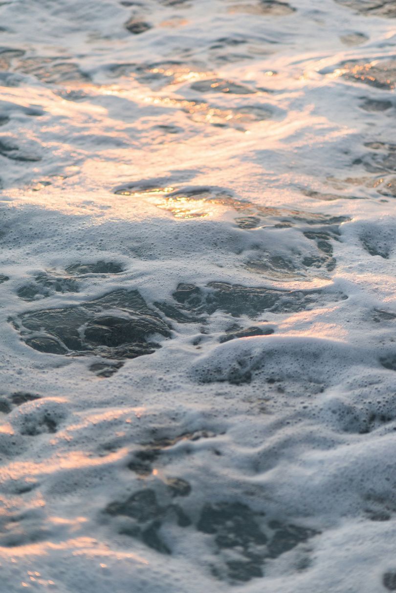 A close up of a beach with waves crashing against the rocks at sunset.