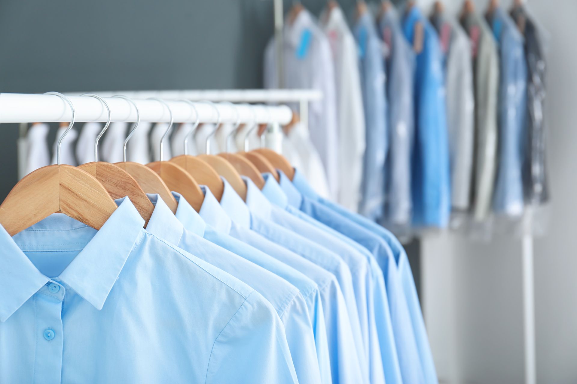 Blue button-up shirts hanging on wooden hangers, rack of laundry.