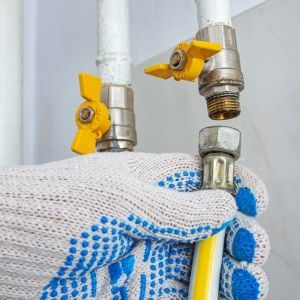 Gloved hand tightening a yellow hose connector under two yellow water shutoff valves