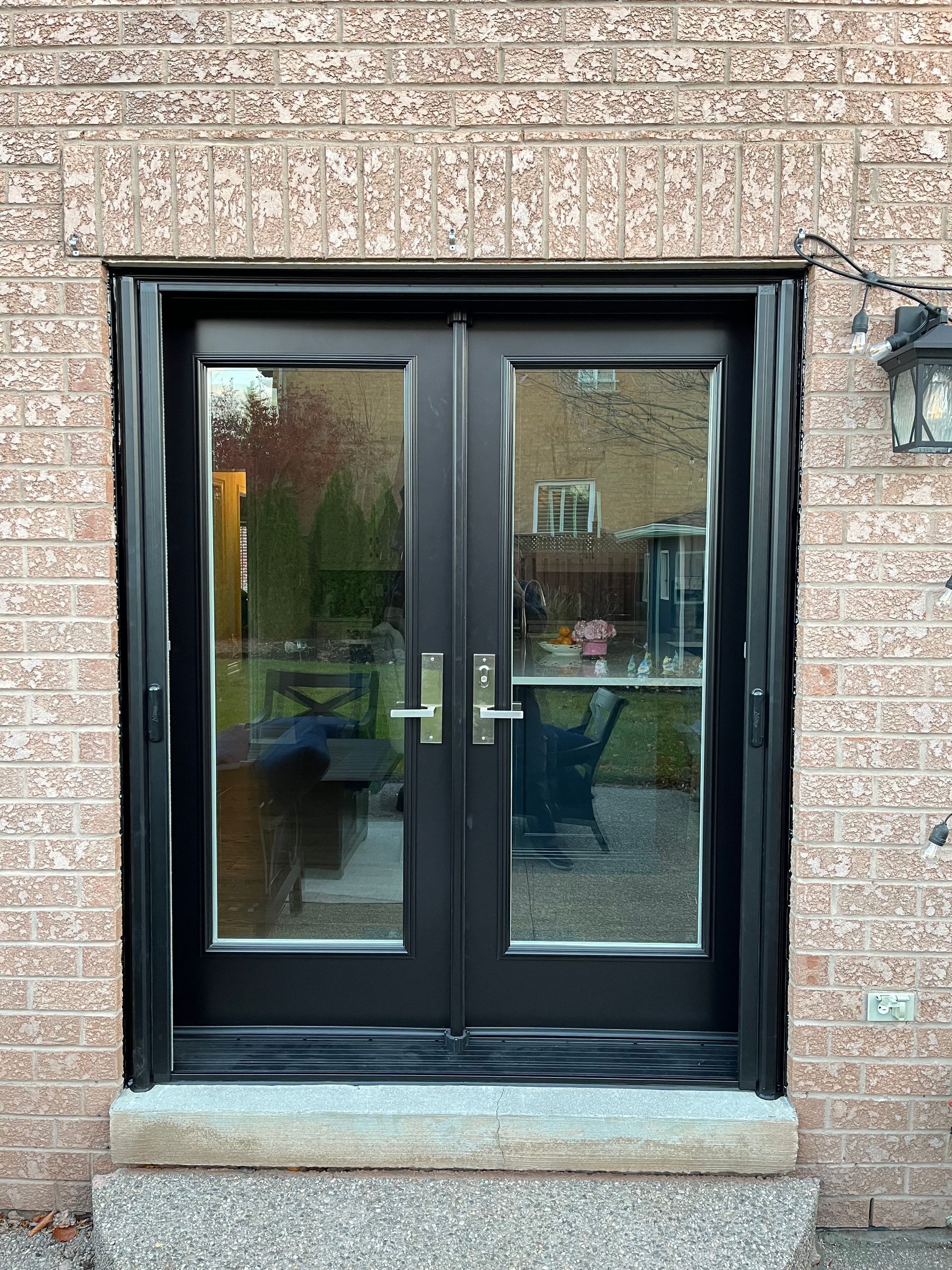 A black double door is sitting on top of a brick wall.