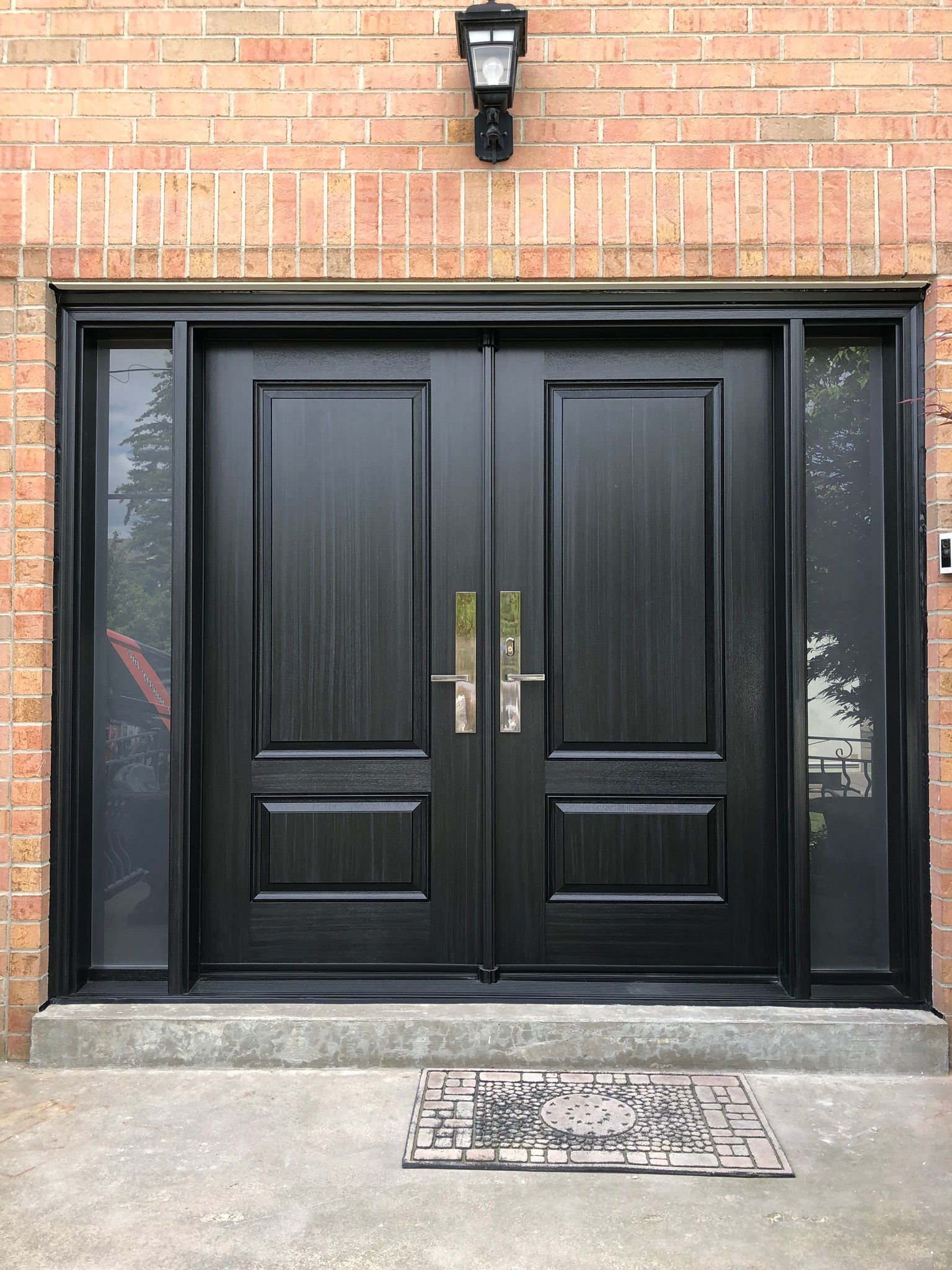 Black double front doors set in a brick building entrance with a wall light above.