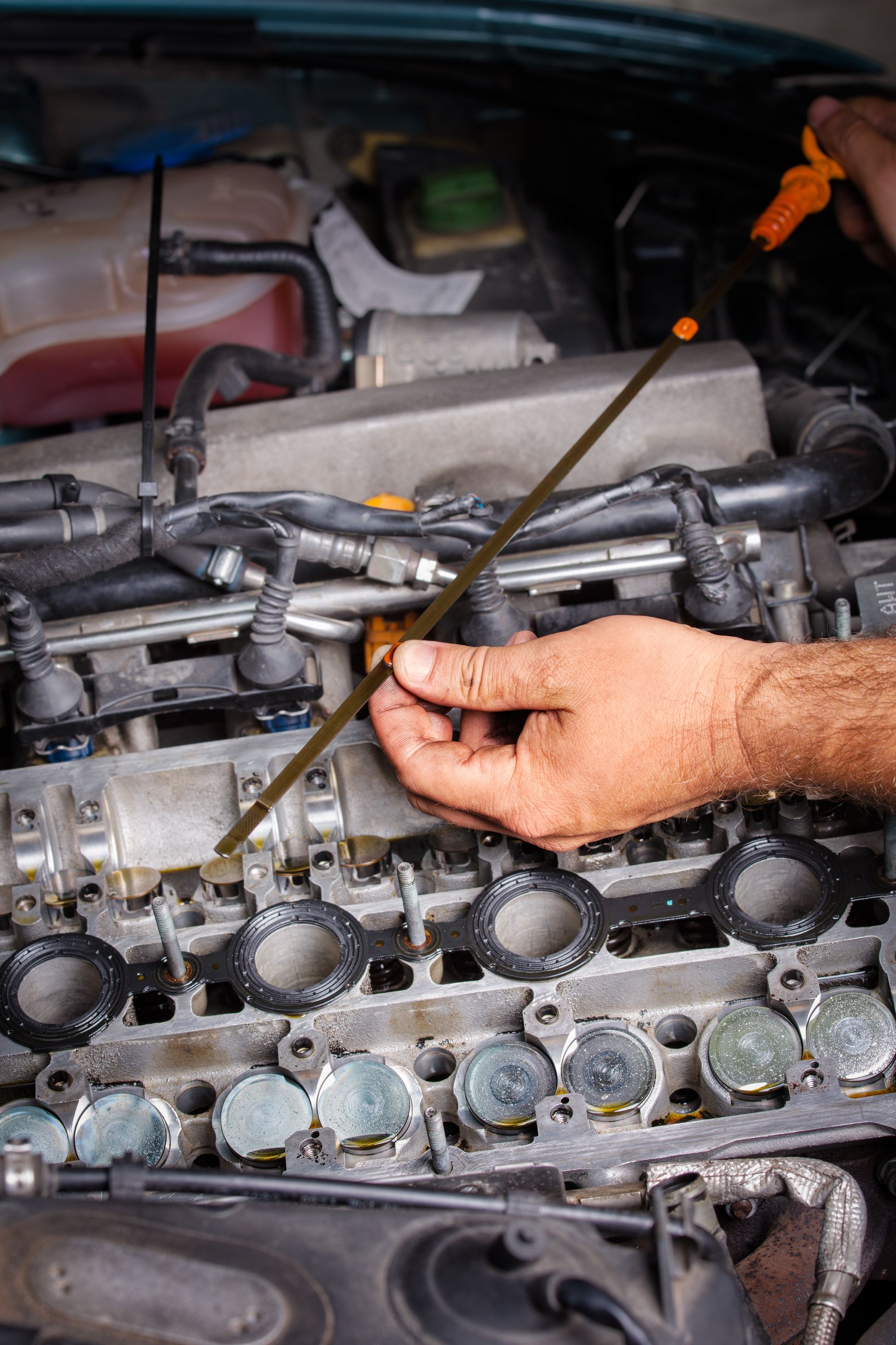 Meccanico che controlla l'olio motore con un'astina di livello all'interno del cofano aperto di un'auto; sono visibili la mano marrone e le parti.