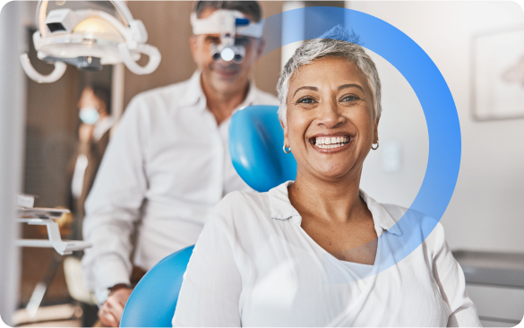 Paciente sorridente em uma clínica odontológica bem iluminada, com um dentista e uma cadeira odontológica azul ao fundo.