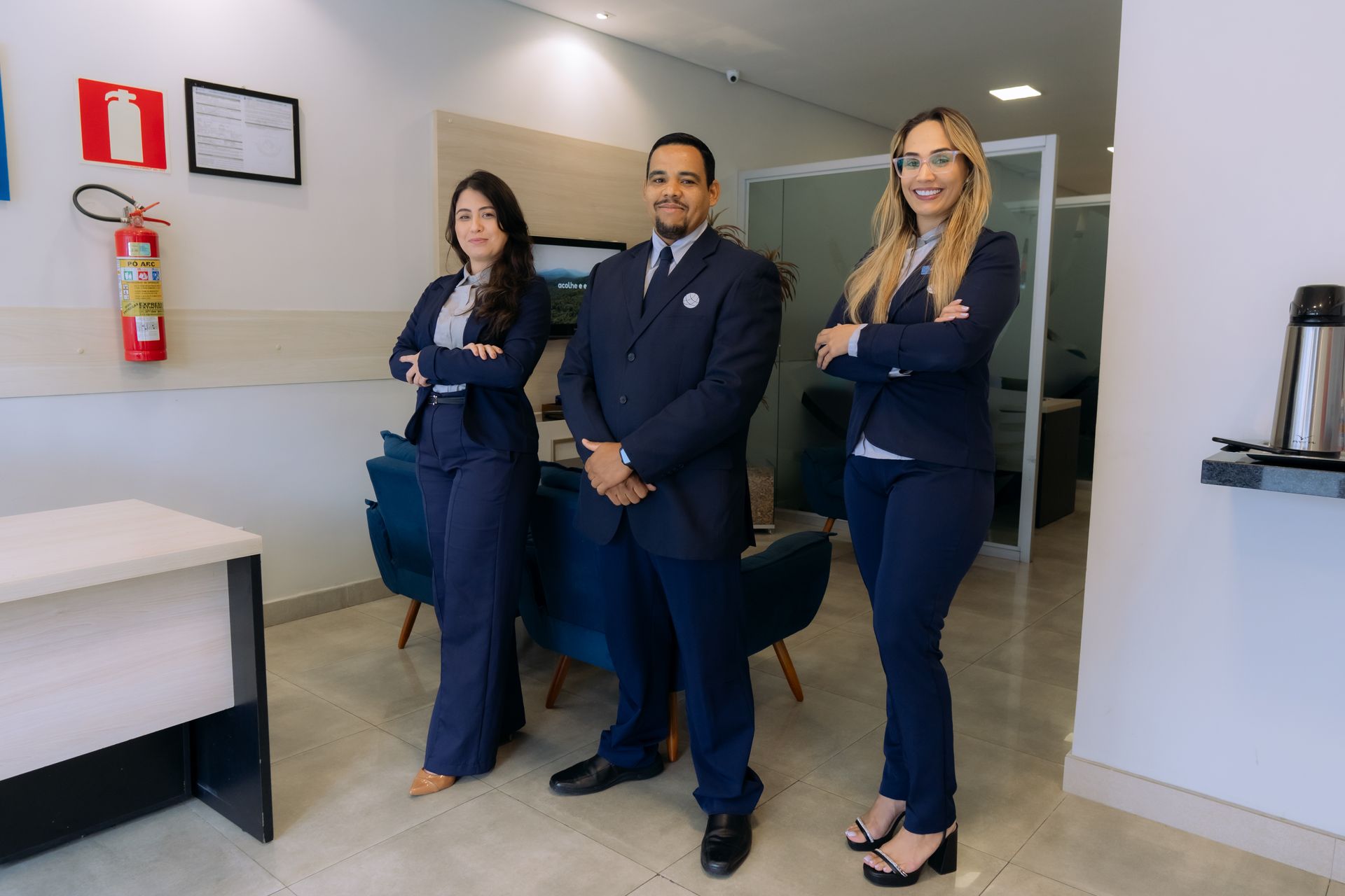 Três pessoas em uniforme da Marinha, de braços cruzados, em um corredor de escritório.