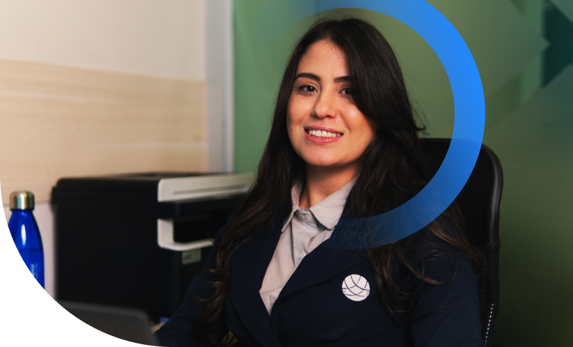 Uma pessoa sorridente, vestindo um blazer escuro, está em pé dentro de casa ao lado de um desenho circular azul.