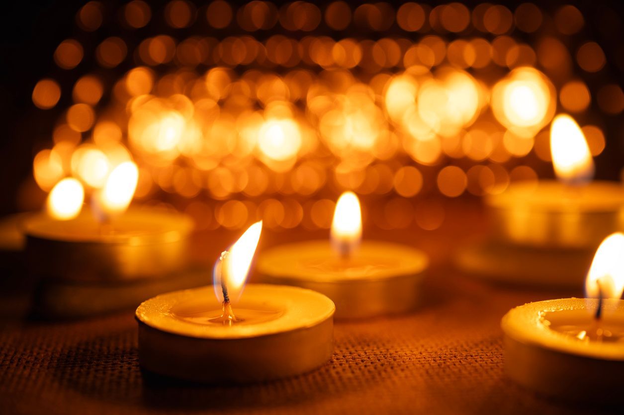 Velas tealight acesas, brilhando em tons quentes de laranja sobre uma superfície escura, com mais velas desfocadas ao fundo.