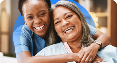 Duas pessoas sorridentes se abraçando em um ambiente interno, uma inclinando-se sobre os ombros da outra.