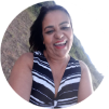 Mulher sorridente com blusa listrada em preto e branco posando contra um fundo claro.