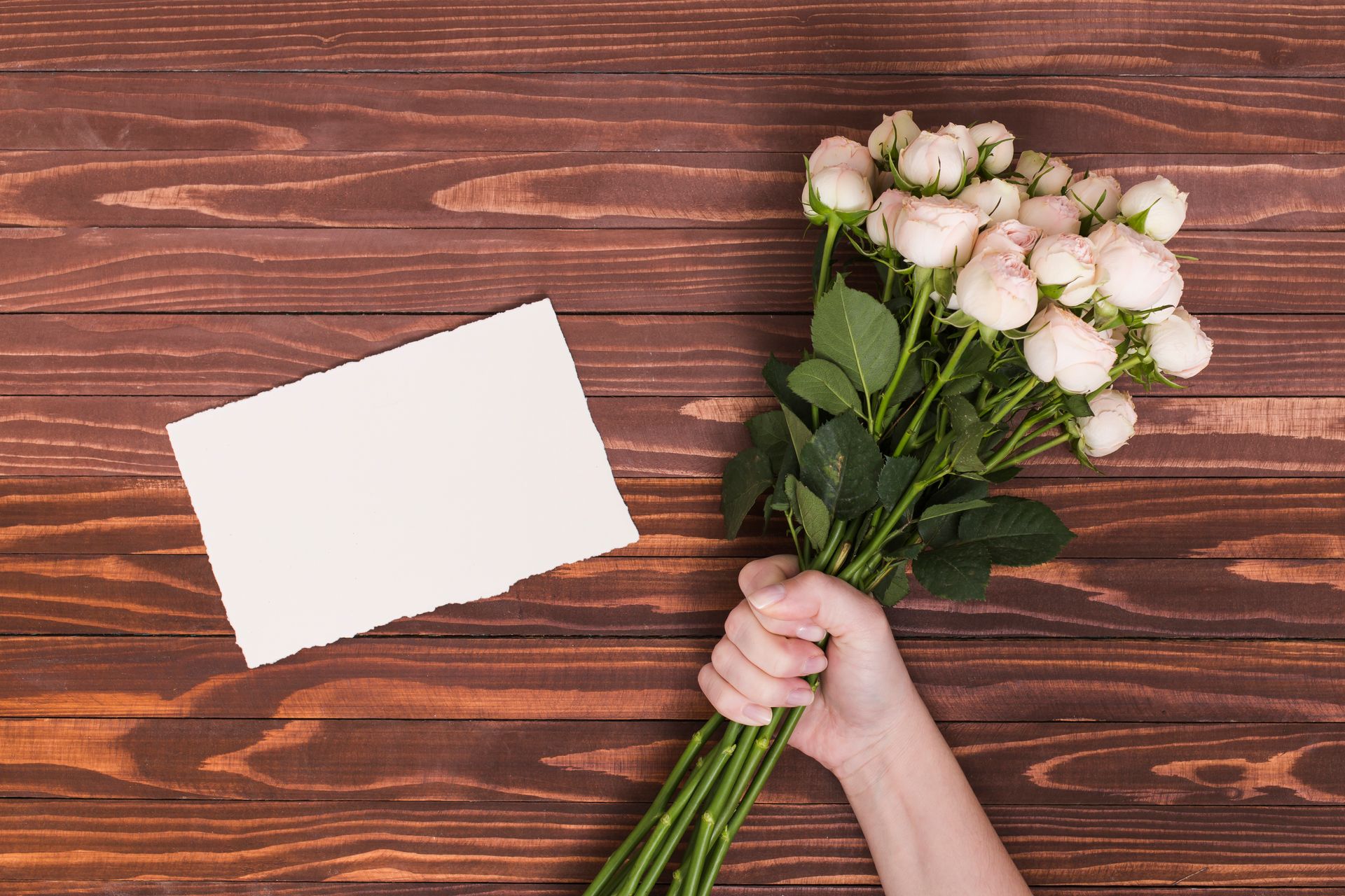 Mão segurando rosas brancas ao lado de um cartão de condolências sobre mesa de madeira