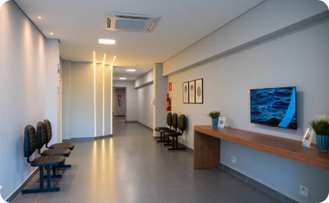 Sala de espera moderna com bancos, balcão, obras de arte na parede e corredor em tons suaves de branco e cinza.