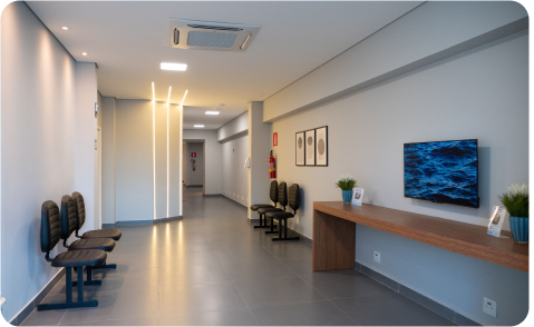 Sala de espera moderna com cadeiras pretas, console de madeira, TV e paredes azul-acinzentadas.