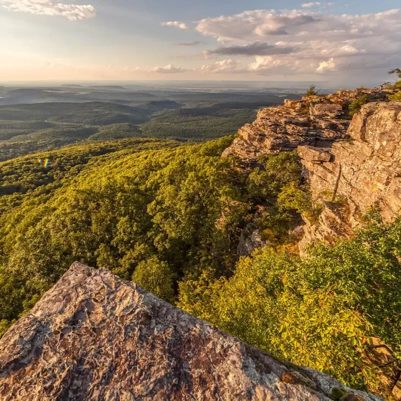 Rocky mountain ridge overlooking a lush green forest at sunset.