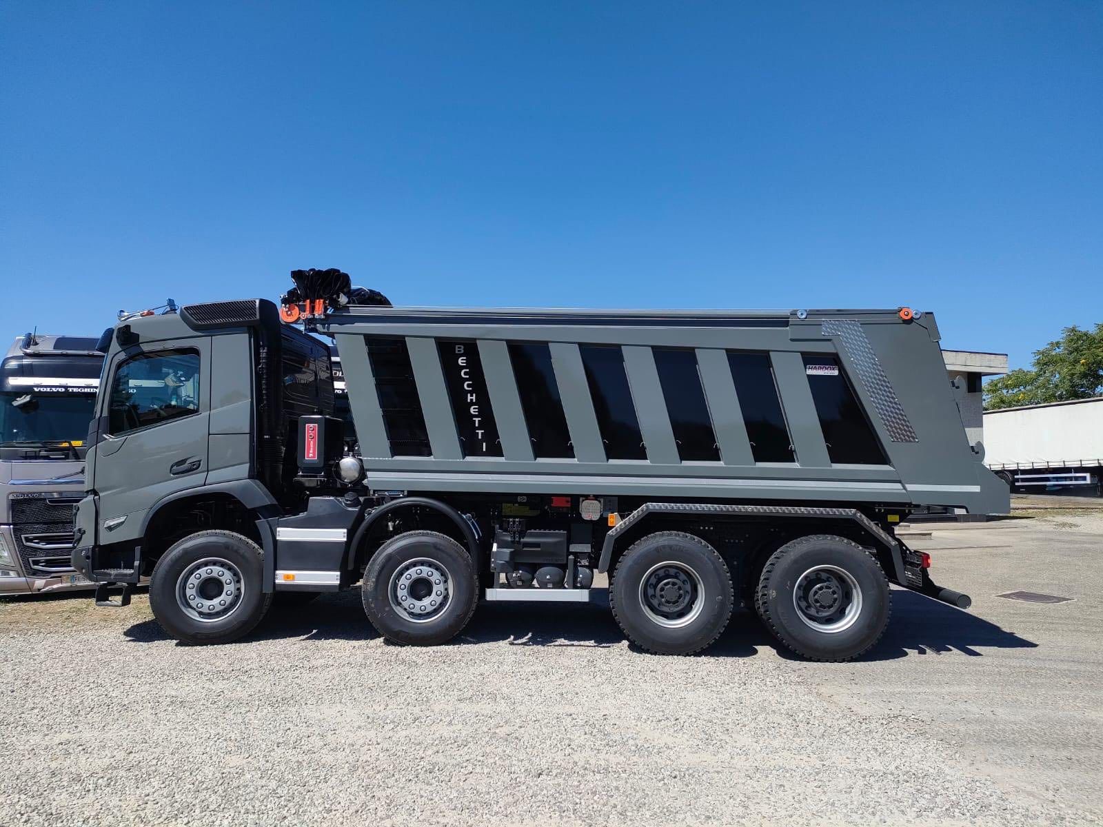 Un camion grigio sulla ghiaia sotto un cielo azzurro.