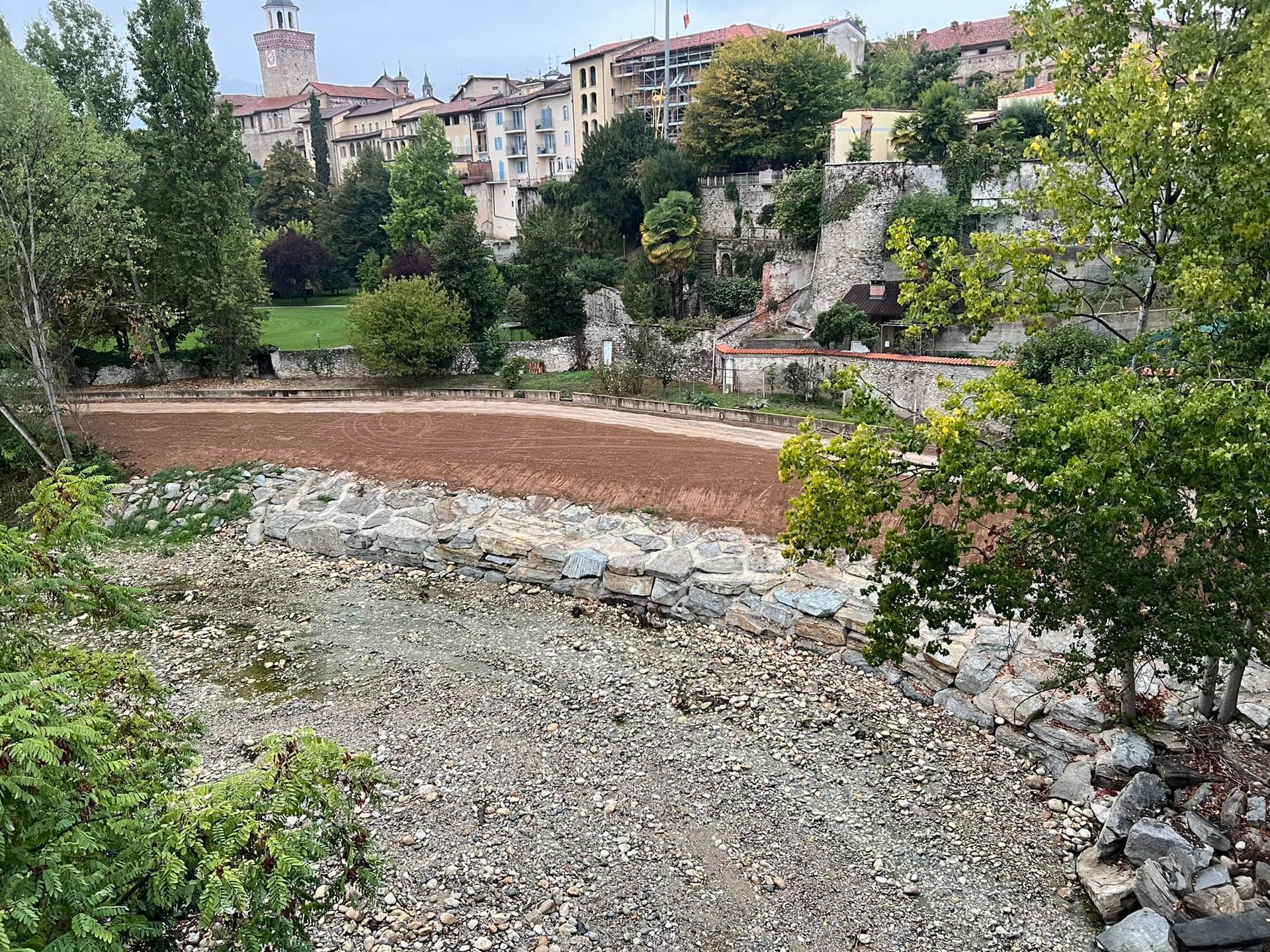 Letto di fiume asciutto con primo piano roccioso, secondo piano marrone e alberi con edifici sullo sfondo.