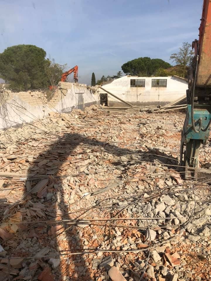 Cantiere demolito con macerie e un escavatore alla luce del sole.