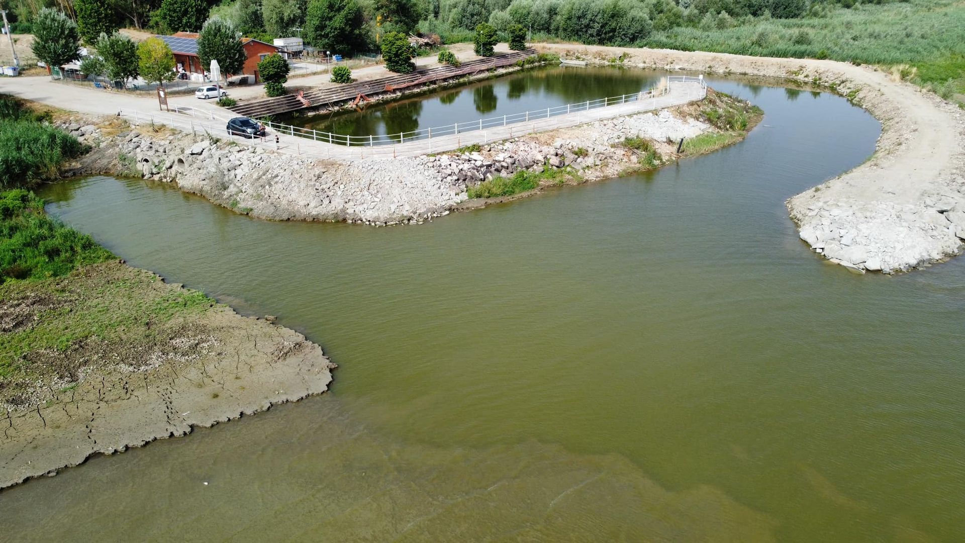 Vista aerea di uno stagno artificiale e di un corso d'acqua con un piccolo complesso edilizio sulla riva.