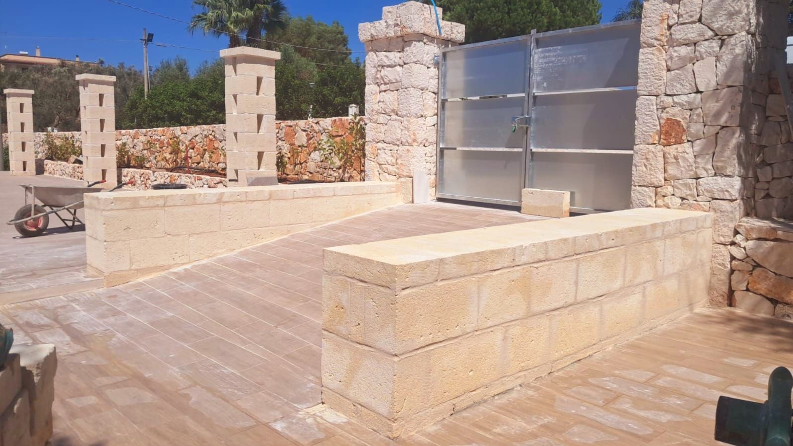 Monumento in pietra all’aperto con muretti e pannelli metallici in un cortile soleggiato