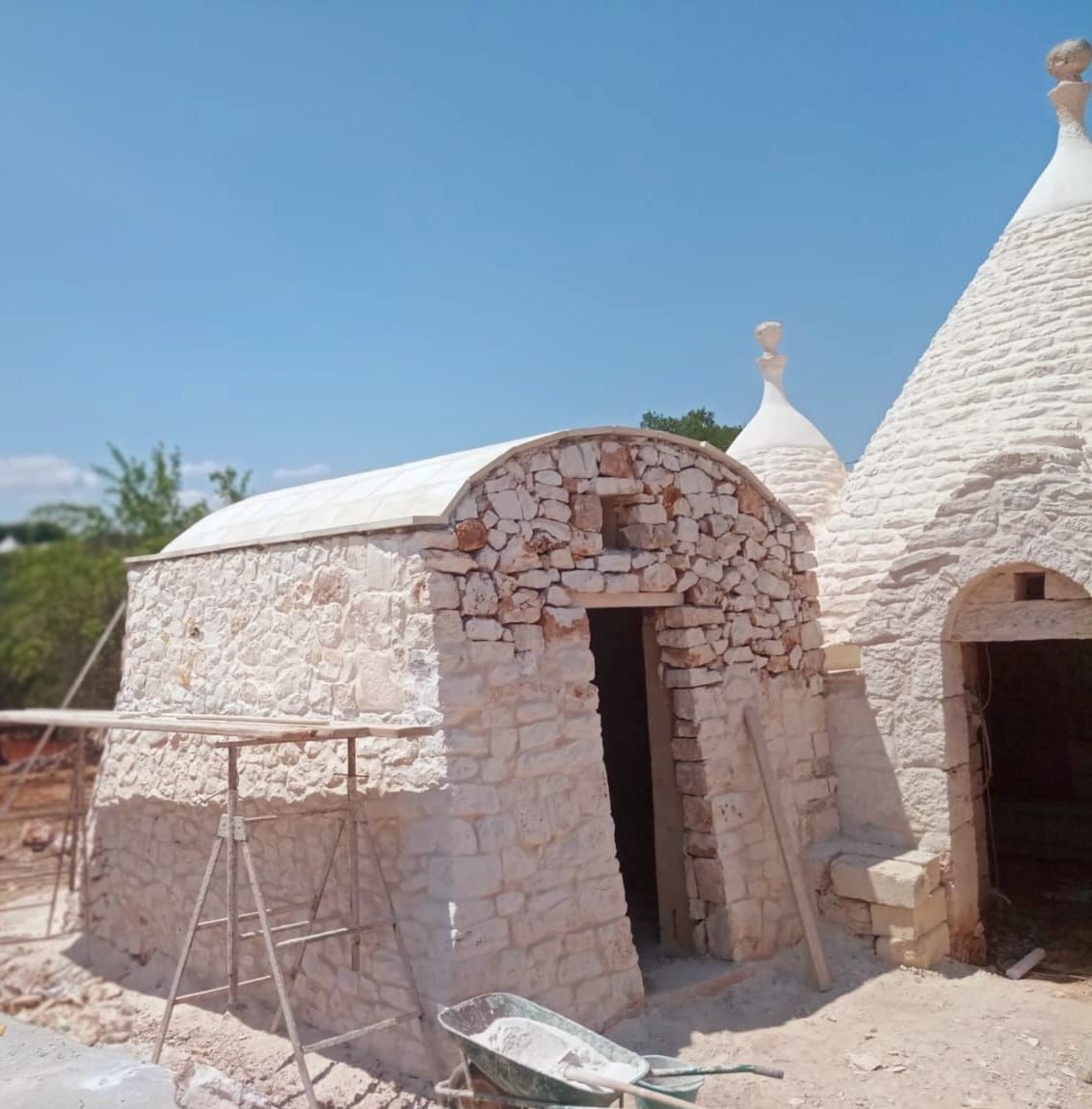 Capanna in pietra con ingresso ad arco e tetto conico bianco sotto un cielo azzurro terso