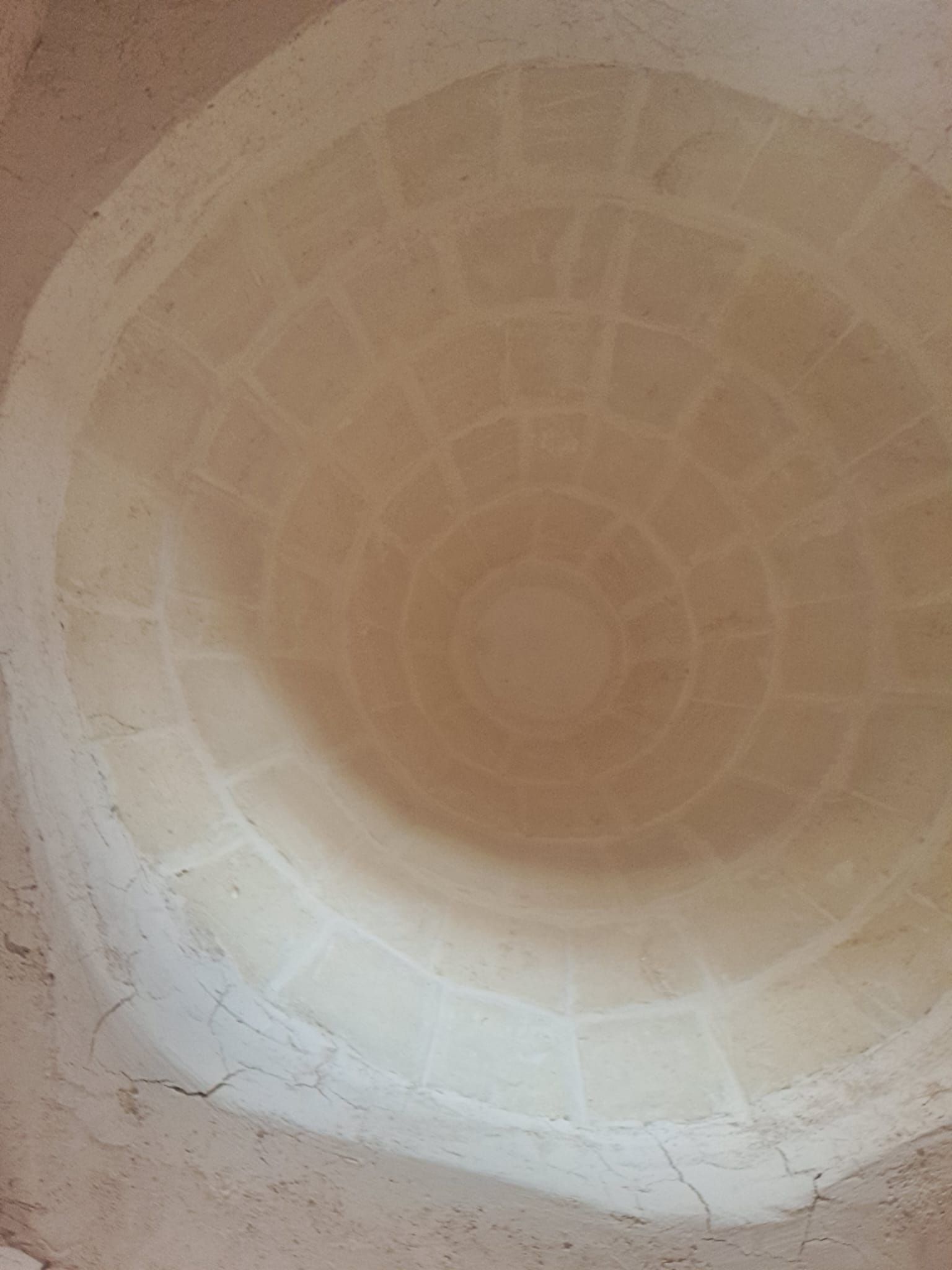 Vista interna di un soffitto a cupola circolare color sabbia, con un motivo geometrico e un’apertura centrale.