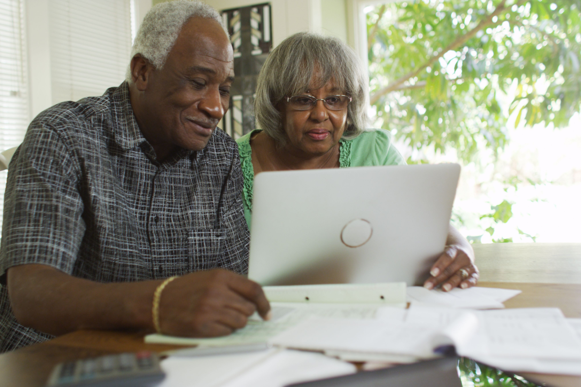 Couple looking at a laptop with papers, indoors near a window.