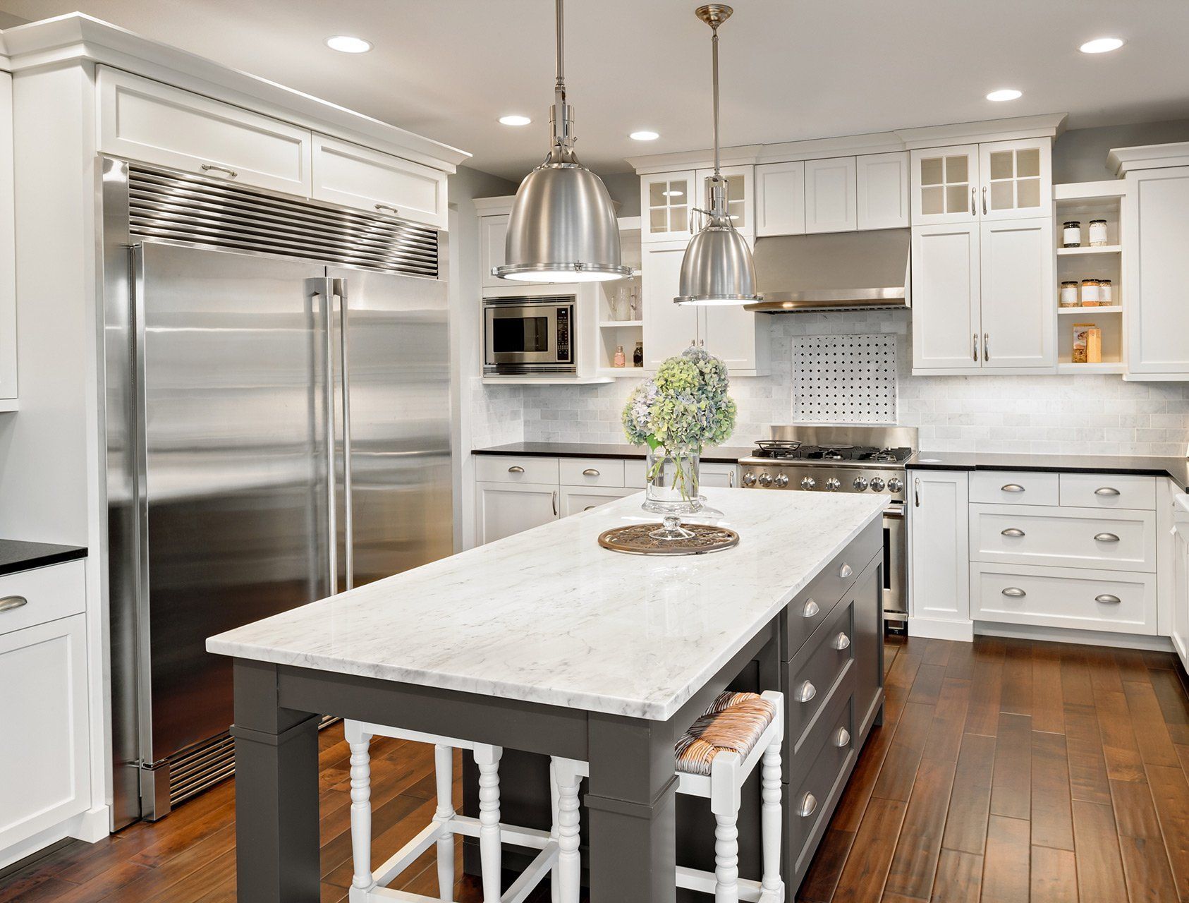 White and gray kitchen with large stainless steel refrigerator, island, and wood floor.