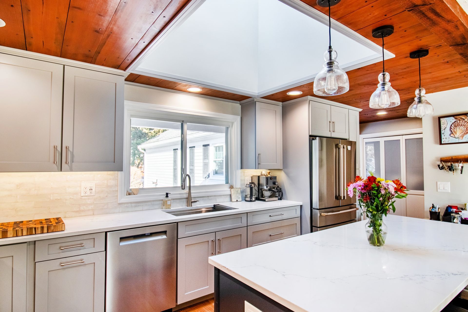 Modern kitchen with gray cabinets, white countertops, stainless steel appliances, and a wood ceiling.