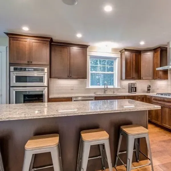Kitchen with brown cabinets, granite countertops, island with stools, and built-in appliances.