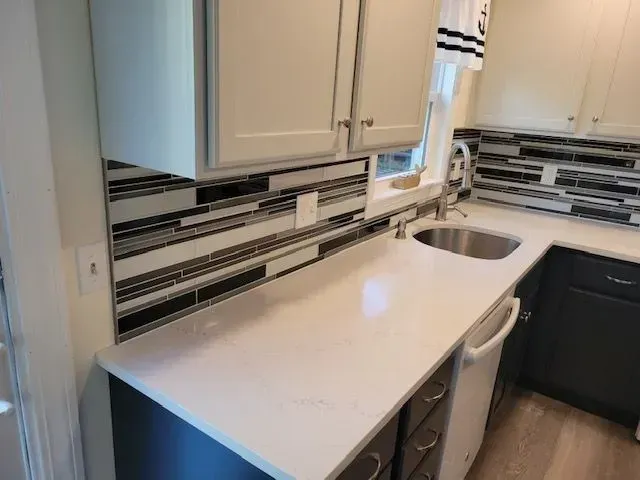 Kitchen with white countertops, dark and light cabinets, and a multi-colored backsplash.