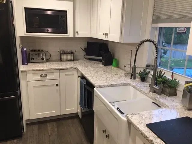 White kitchen with granite countertops, farmhouse sink, microwave, and a window.