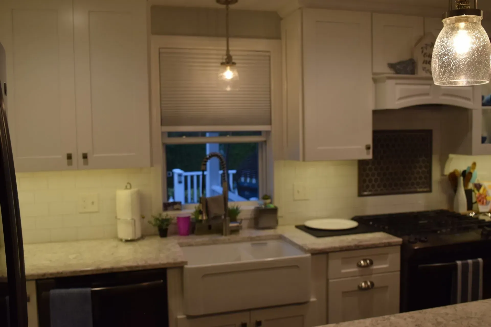 White kitchen with window, sink, cabinets, and a hanging light.