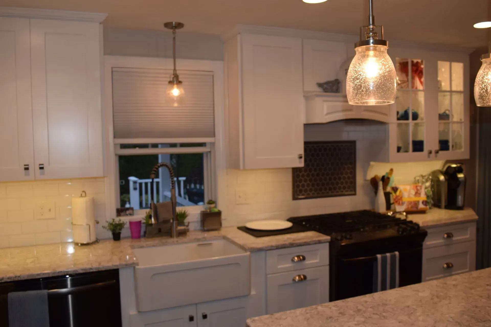 White kitchen with cabinets, sink, and stovetop, under a hanging light.