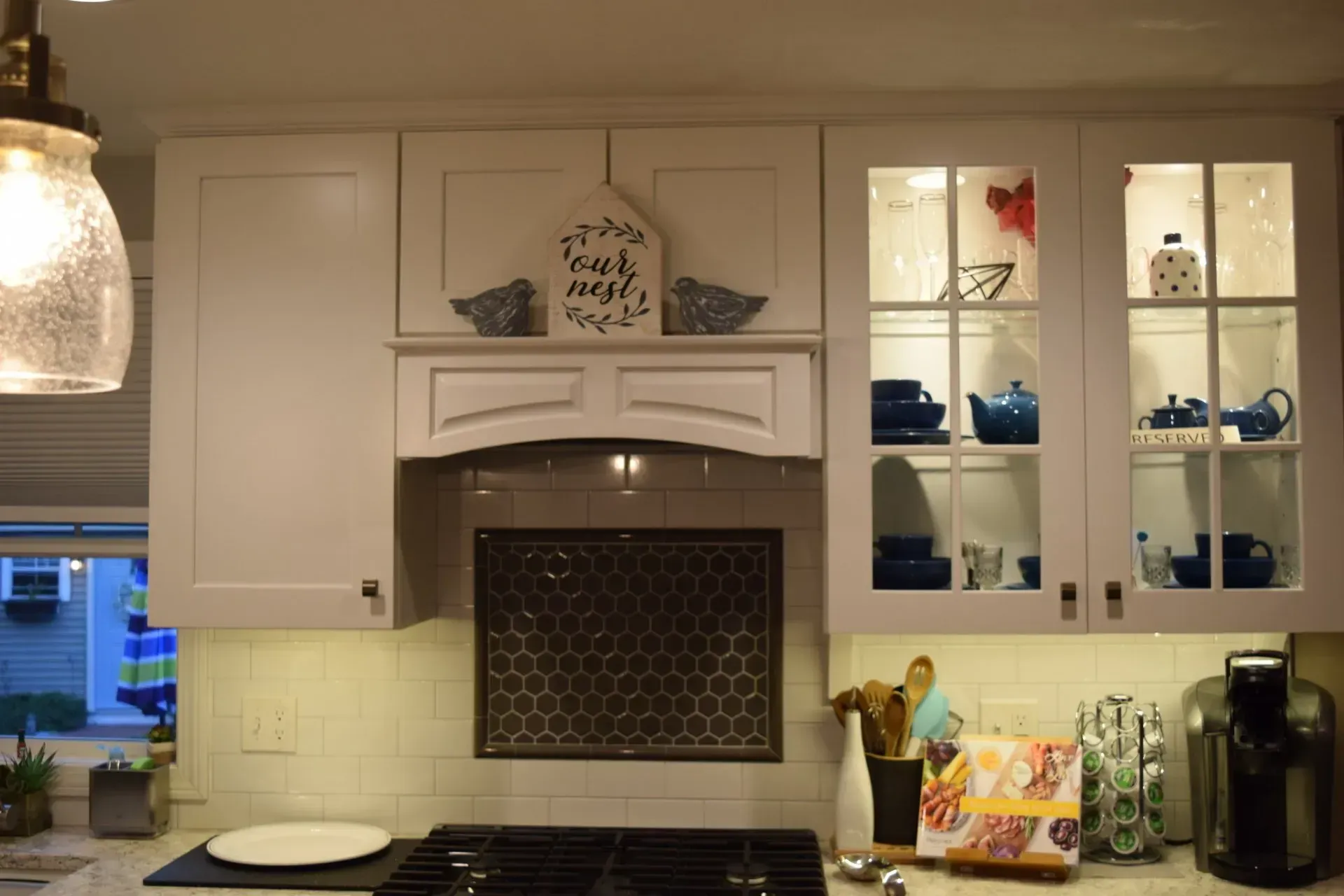 White kitchen cabinets with glass-front display, above a stovetop and range hood; teal accents.