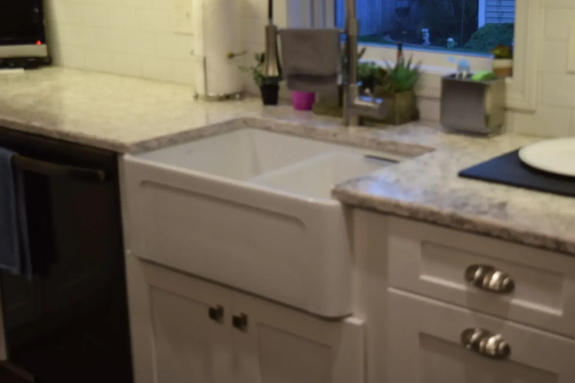 White farmhouse kitchen sink with stainless steel faucet. Granite countertops, white cabinets.