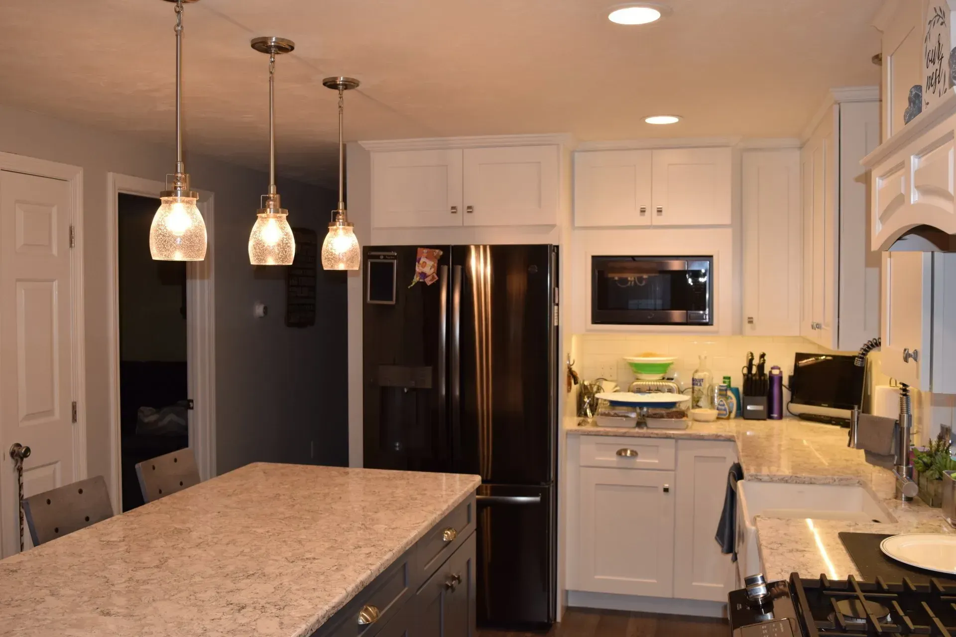 Kitchen with white cabinets, dark refrigerator, island with pendant lights.