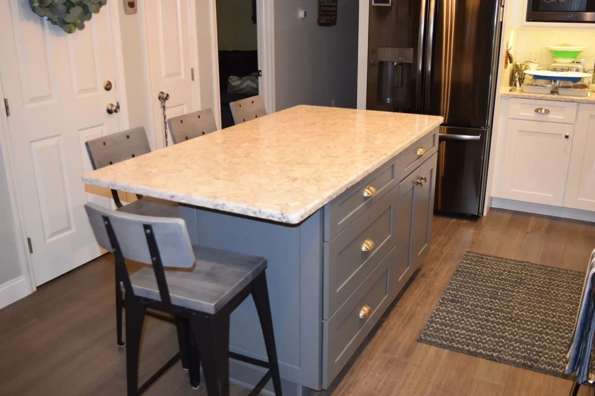 Kitchen island with granite countertop, gray cabinets, bar stools, and refrigerator.
